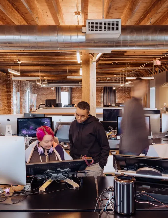 Row of artist work bays in a creative studio with desks, monitors, and task lighting