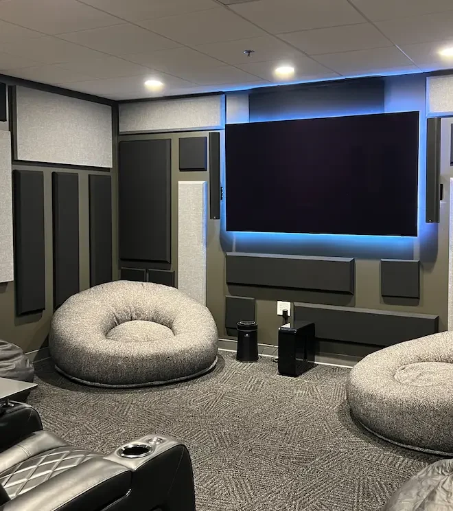 Premium media room with acoustic panels, large wall-mounted display, lounge seating, and integrated AV equipment installed by Macrotek.