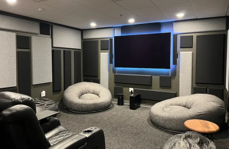 Premium media room with acoustic panels, large wall-mounted display, lounge seating, and integrated AV equipment installed by Macrotek.