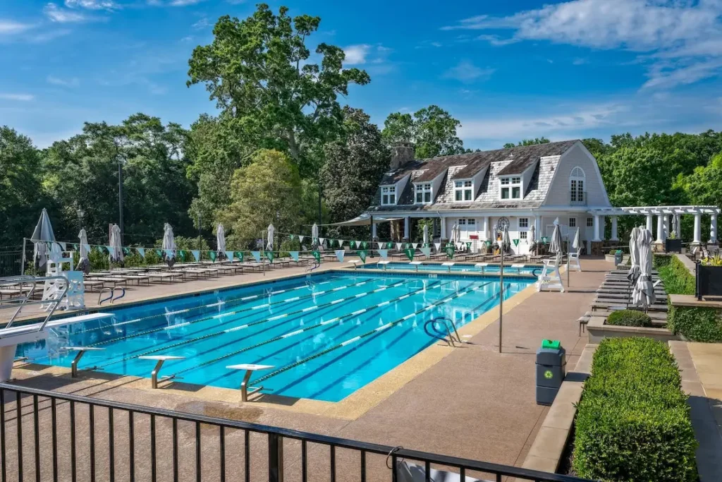 Outdoor lap pool with diving boards, lane lines, and lounge chairs in front of a clubhouse at a private golf club