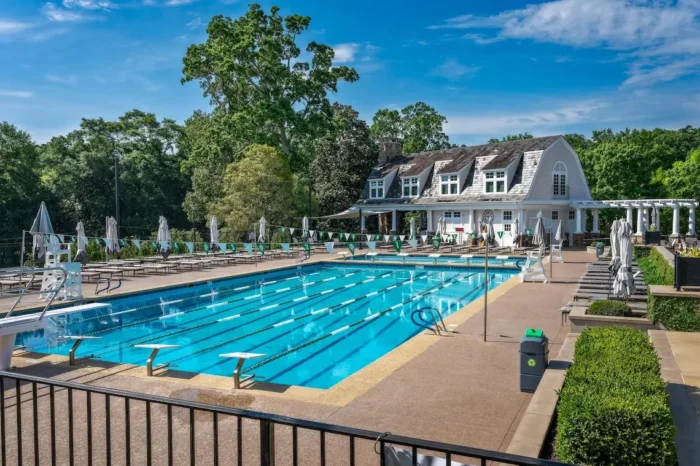 Outdoor lap pool with diving boards, lane lines, and lounge chairs in front of a clubhouse at a private golf club