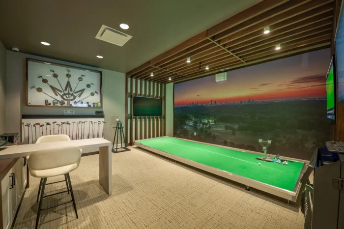 Indoor golf training center with putting green, practice stations, and wall graphics at a private club