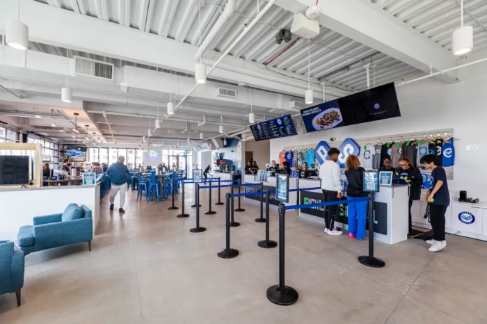 Bright lobby and concessions area at an indoor entertainment venue with digital menu boards, queue stanchions, and seating