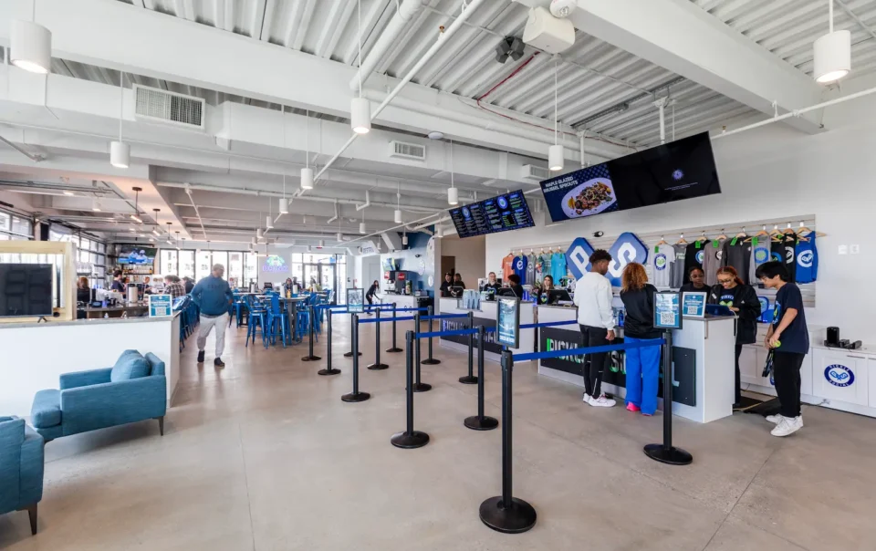 Bright lobby and concessions area at an indoor entertainment venue with digital menu boards, queue stanchions, and seating