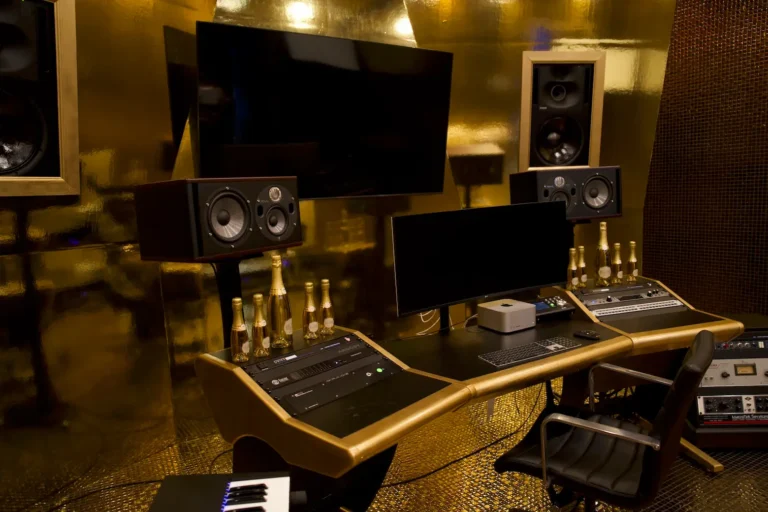 Gold-walled recording studio mix position with monitors, speakers, and audio racks