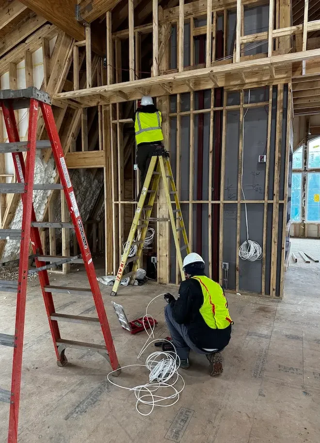 Two technicians in safety vests running low voltage cabling inside a new building under construction
