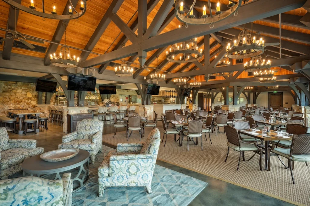 Private club lounge at Capital City featuring Macrotek Services AV setup for club events—ceiling-mounted speakers, wall-mounted digital displays, and ambient chandeliers beneath exposed timber trusses.