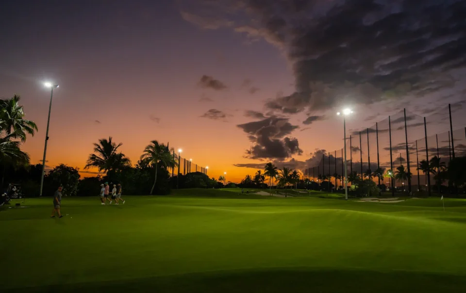 Practice area with distributed audio system along driving range illuminated at twilight